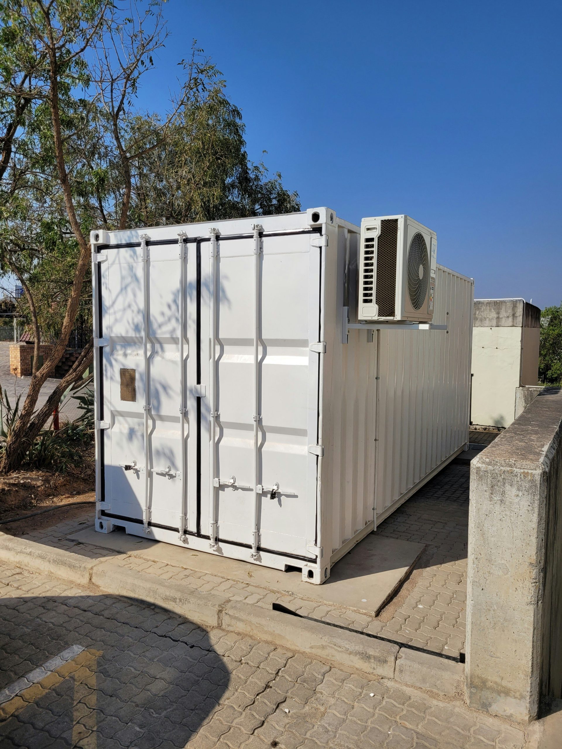 White shipping container with an external air conditioning unit.